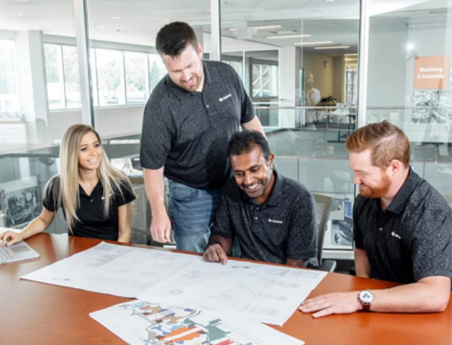 Four colleagues collaborate around a table, reviewing architectural blueprints in a modern office setting.