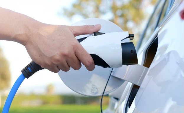 Electric vehicle charging port with a hand plugging in a charging cable outdoors.