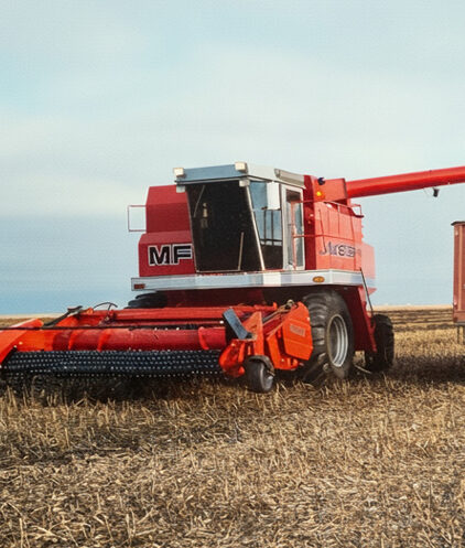 Red Massey Ferguson combine harvester working in a dry wheat field under a cloudy sky.