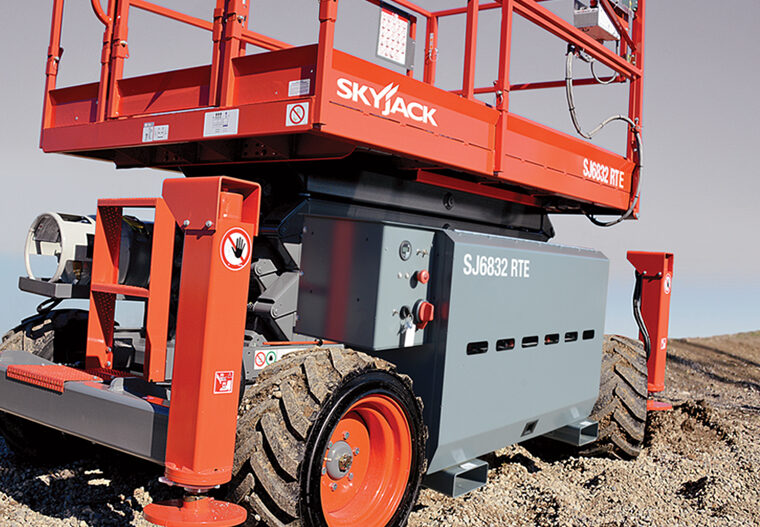 Close-up of a red and gray Skyjack scissor lift with large rugged tires on a gravel surface.