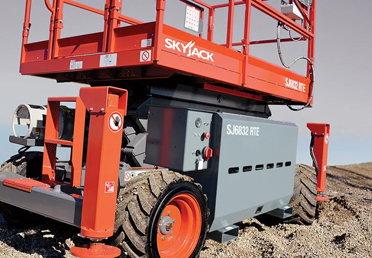 Close-up of a red and gray Skyjack scissor lift with large rugged tires on a gravel surface.