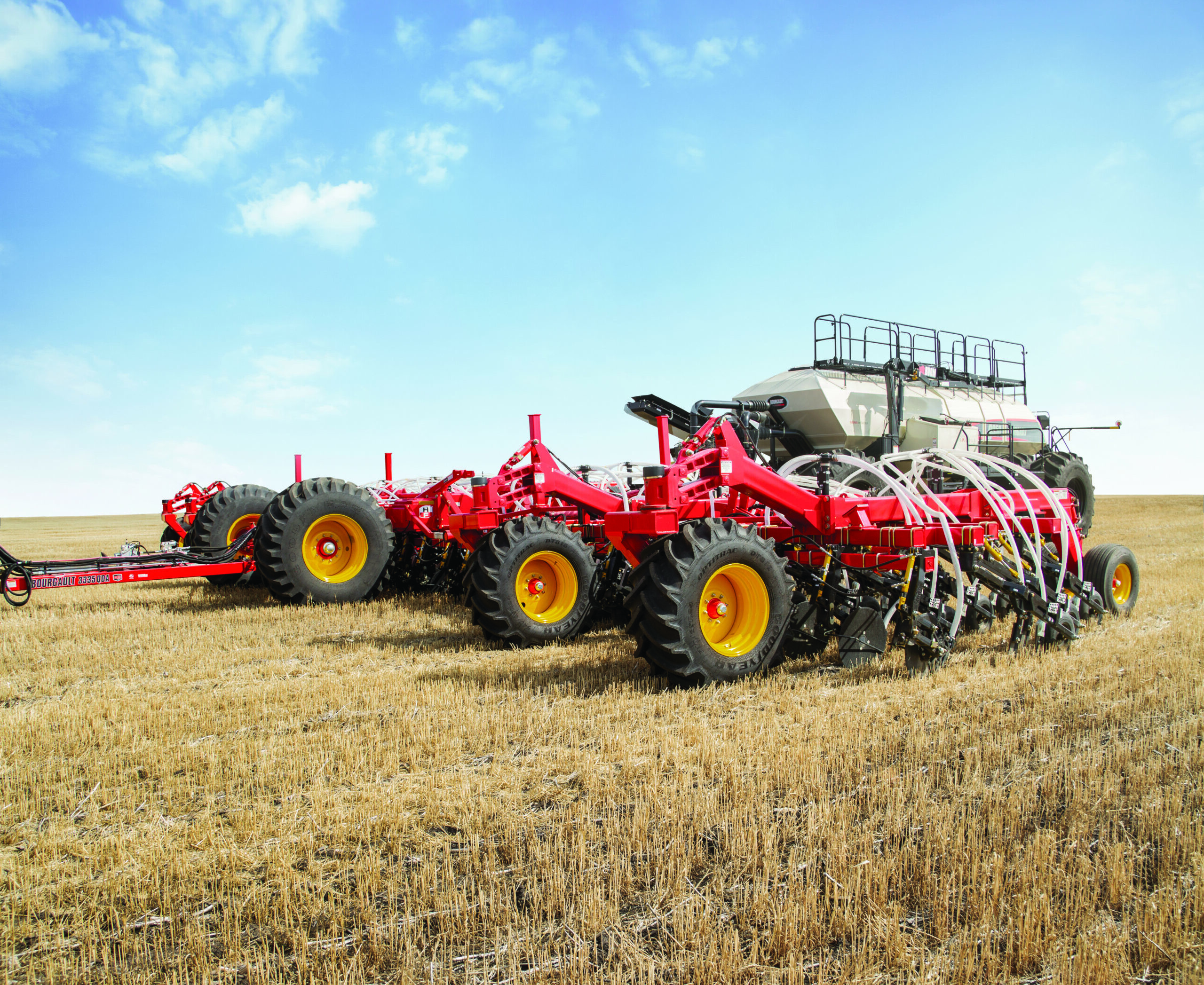 Red agricultural planter machine with multiple seed drills working on a harvested field under a clear blue sky.