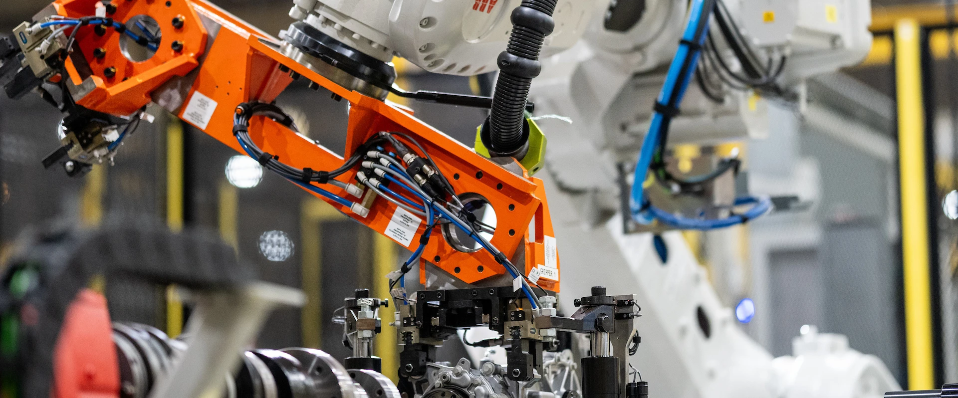 Close-up of an orange industrial robotic arm assembling components in a high-tech manufacturing facility.
