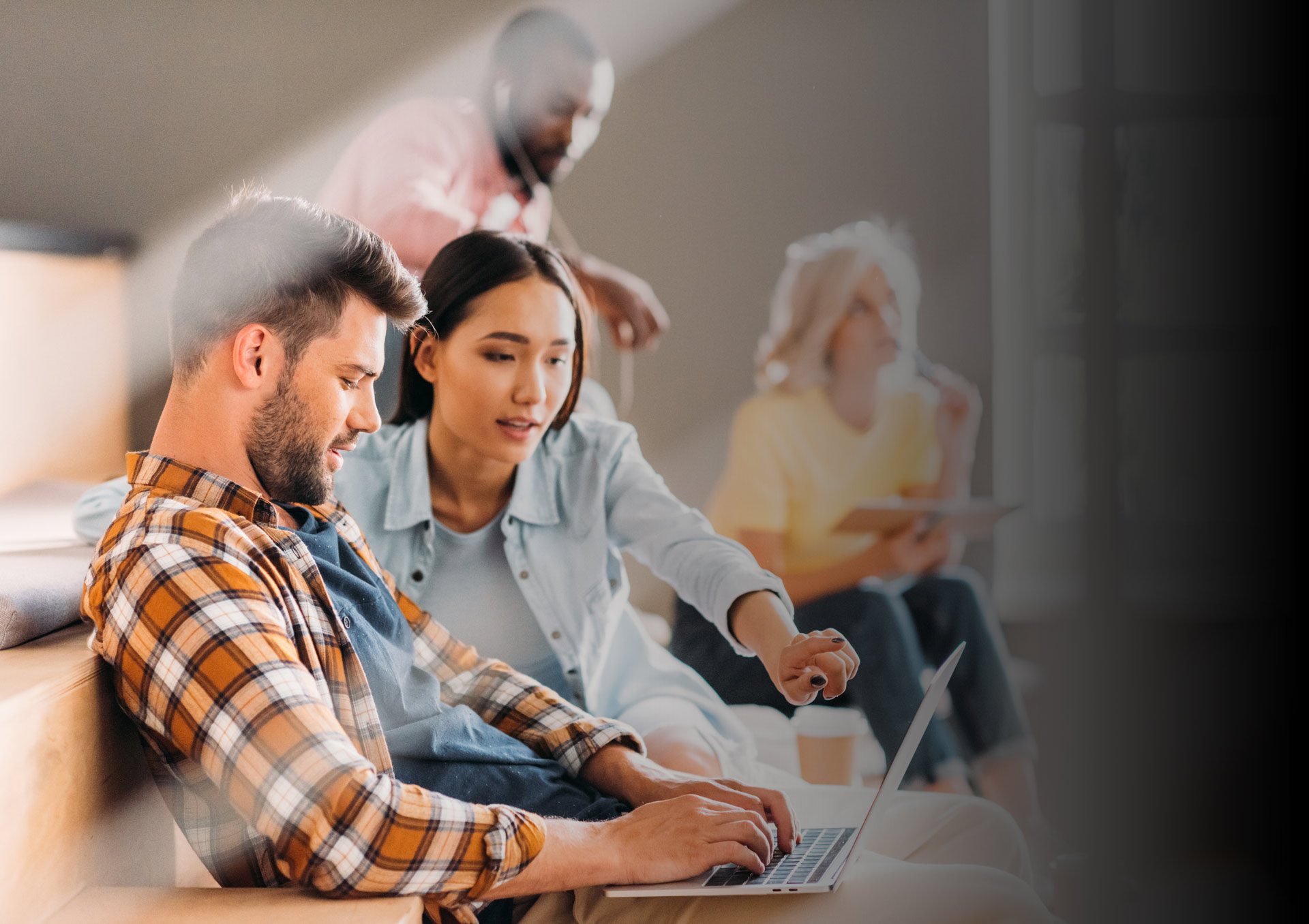 A diverse group of young professionals collaborating and working on laptops in a modern office environment.