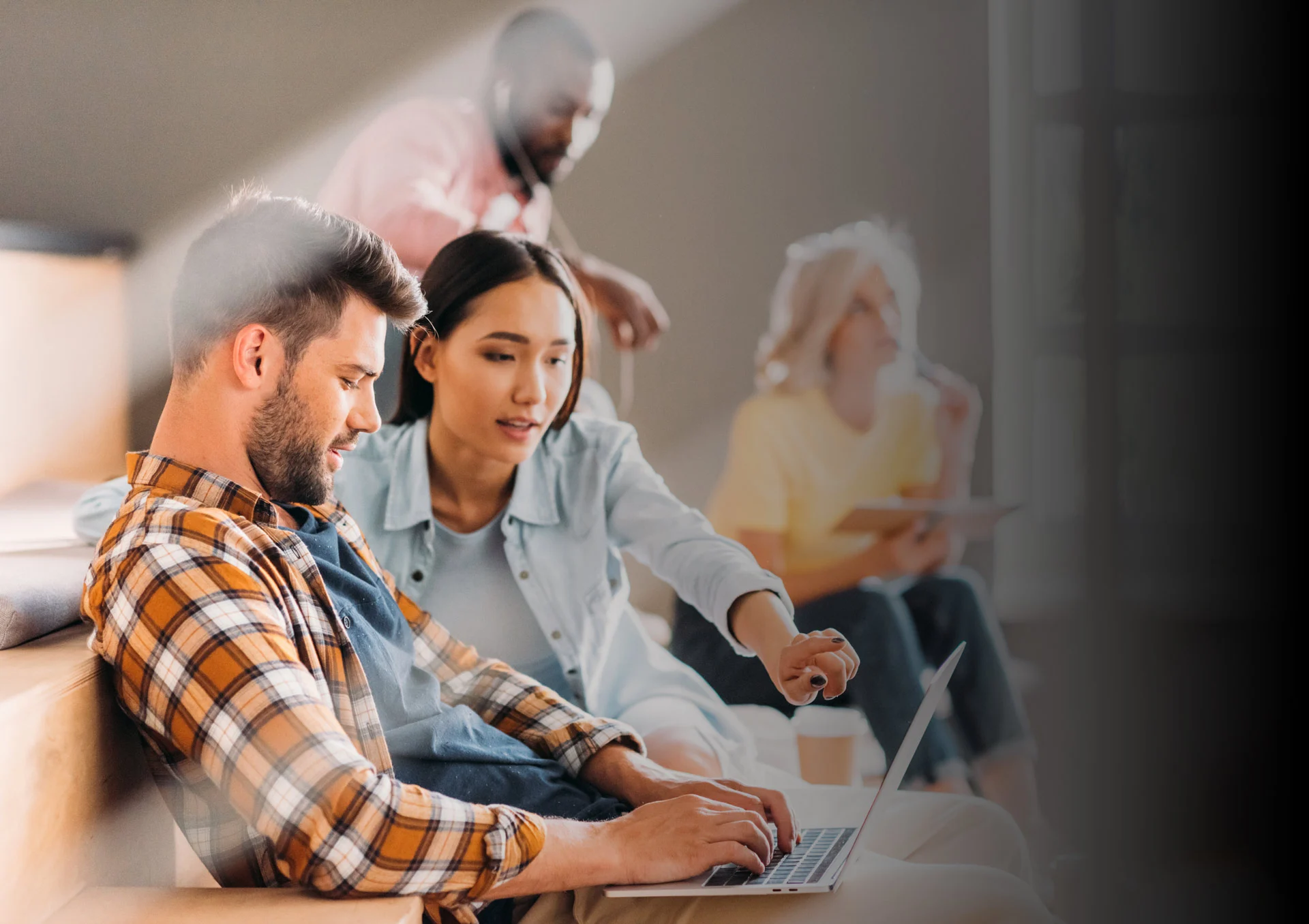 A diverse group of young professionals collaborating and working on laptops in a modern office environment.