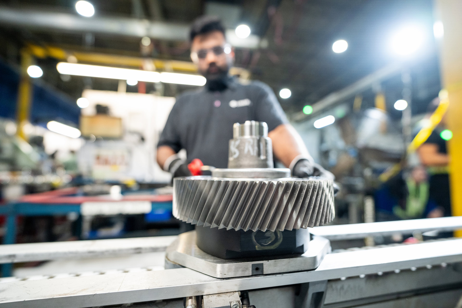 Close-up of a technician inspecting a large industrial gear in a factory setting with blurred background machinery.