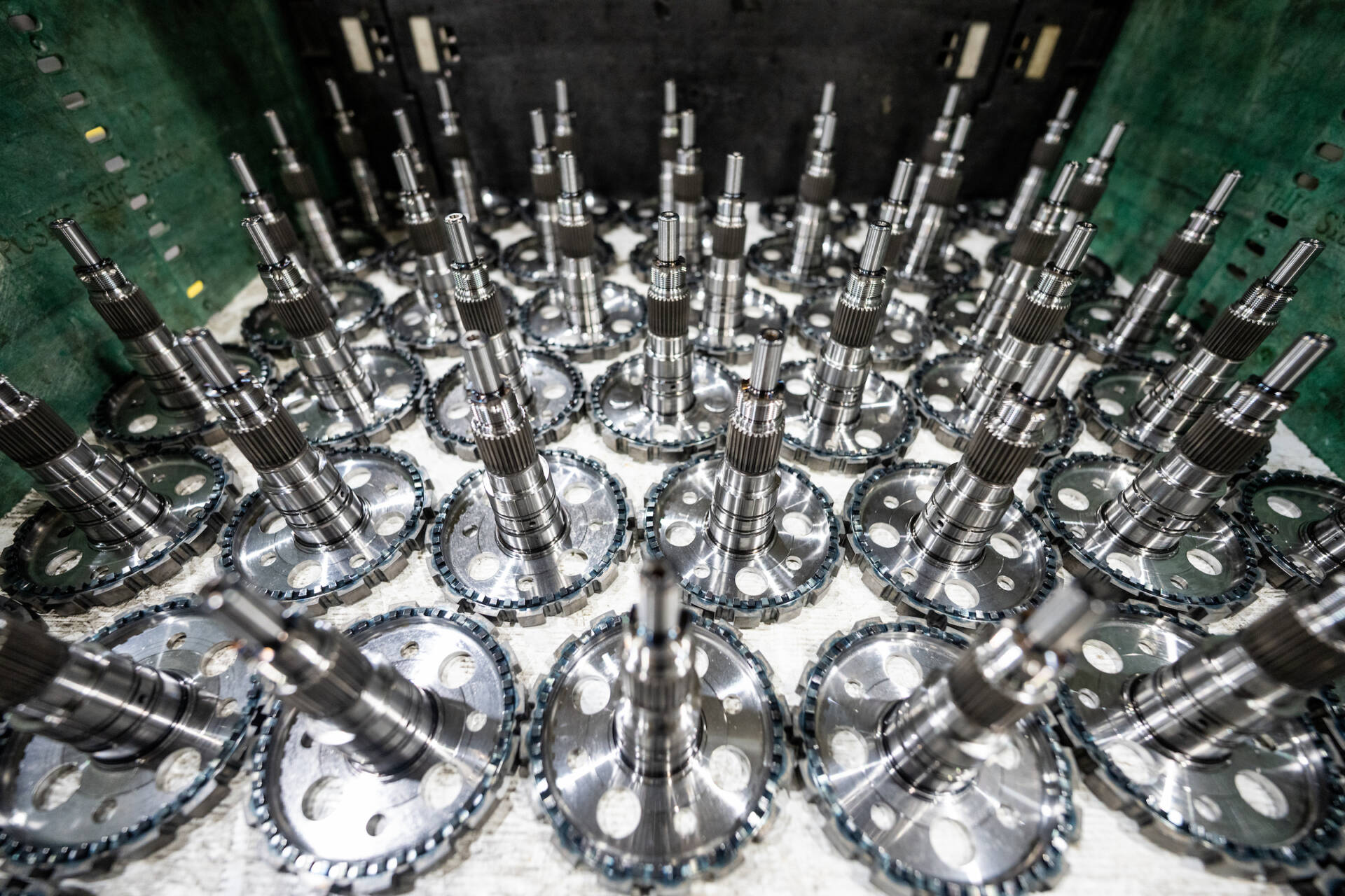 A close-up view of multiple shiny, metallic industrial gears or mechanical components arranged in a circular pattern on a green surface.