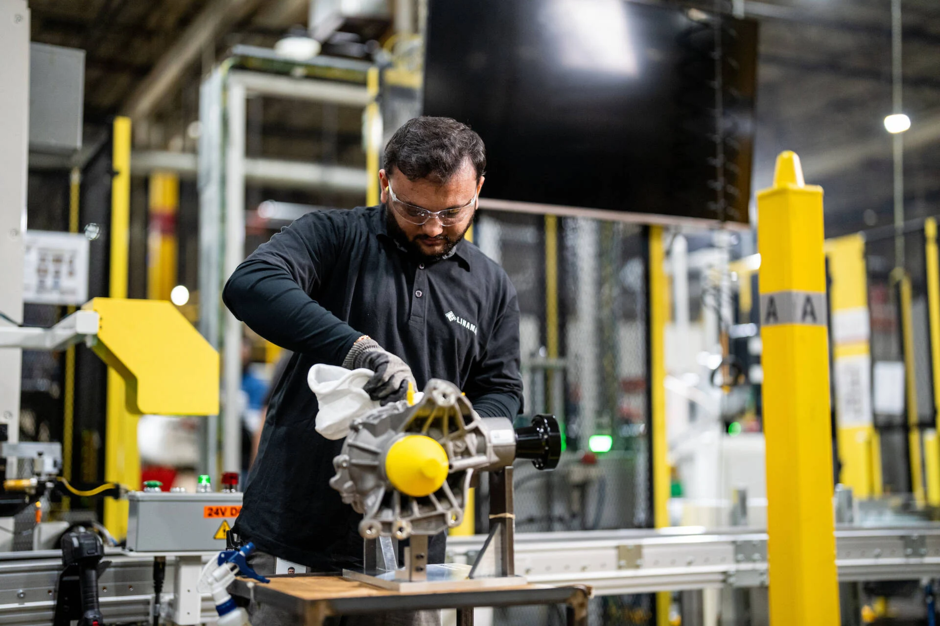 Man wearing safety glasses and gloves operating machinery in an industrial manufacturing facility.