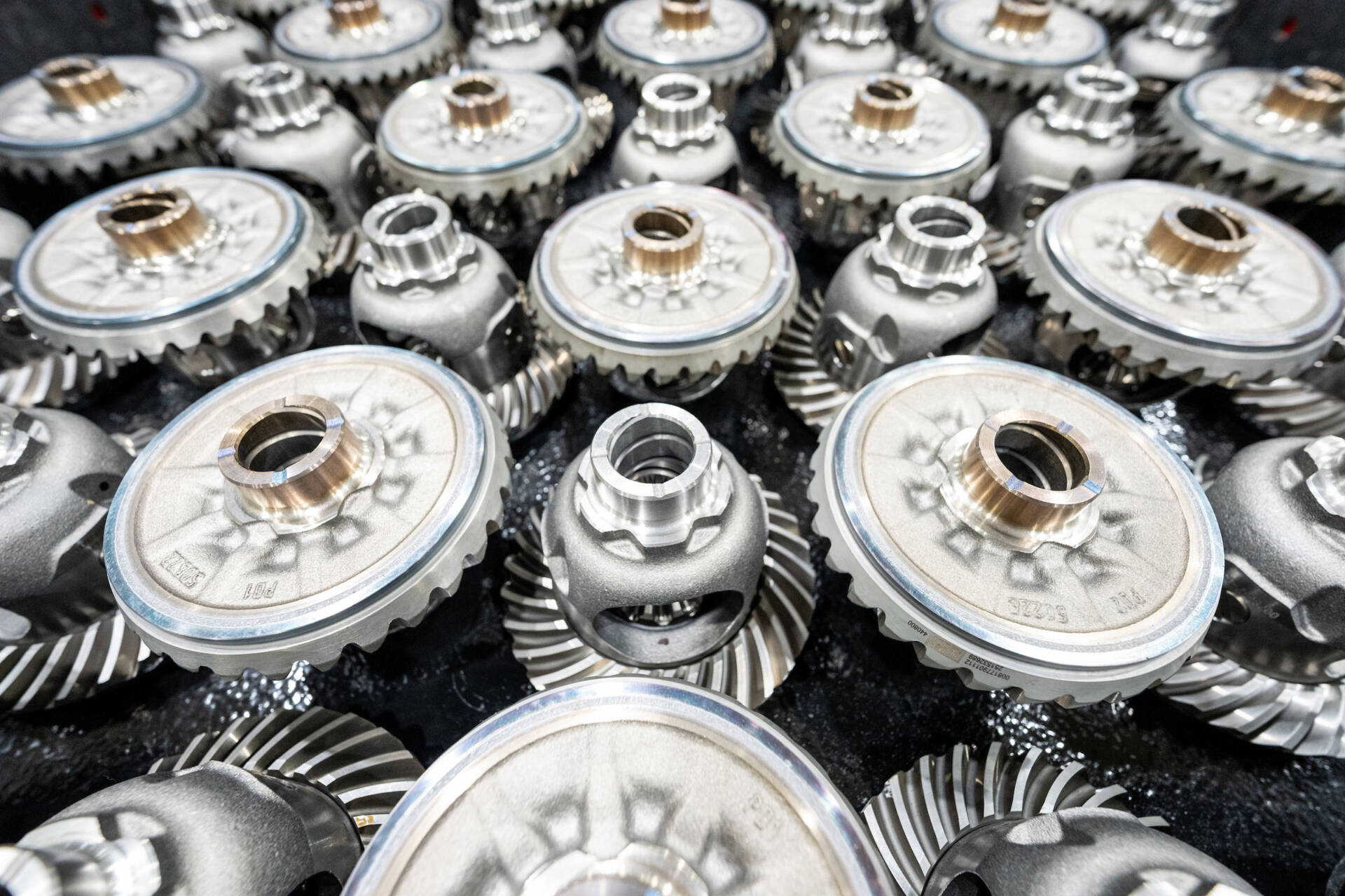 Close-up of multiple silver mechanical gears with intricate detailing, arranged in a dense pattern.