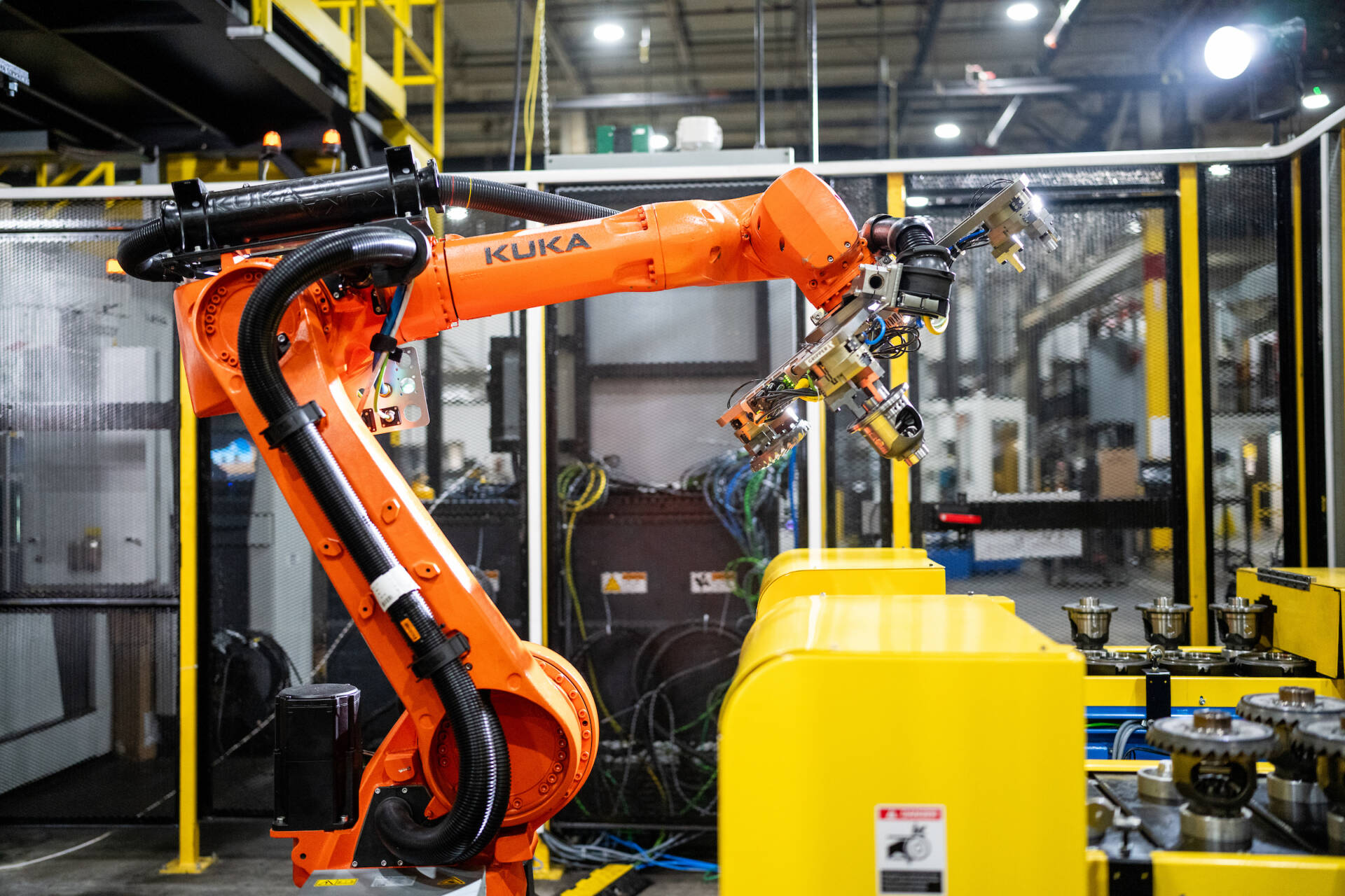 Orange industrial robotic arm operating inside a modern automated manufacturing facility.