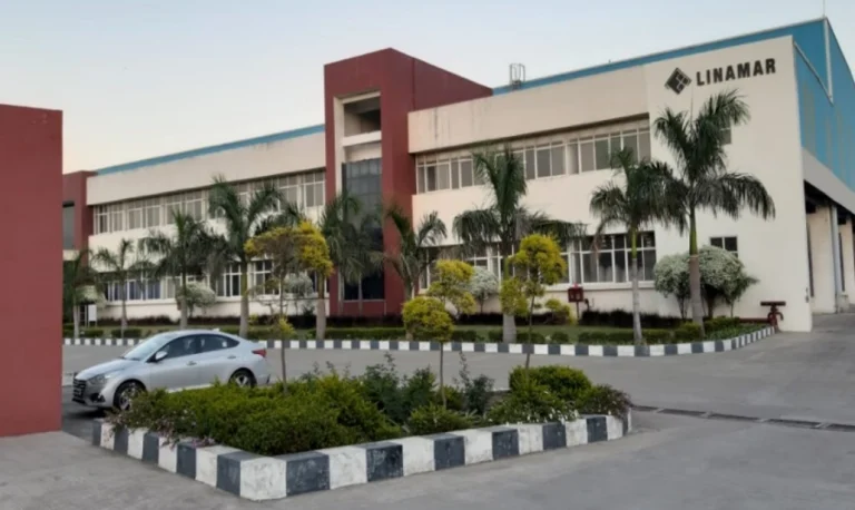 Modern multi-story office building with palm trees and parked cars in front, captured during daylight.