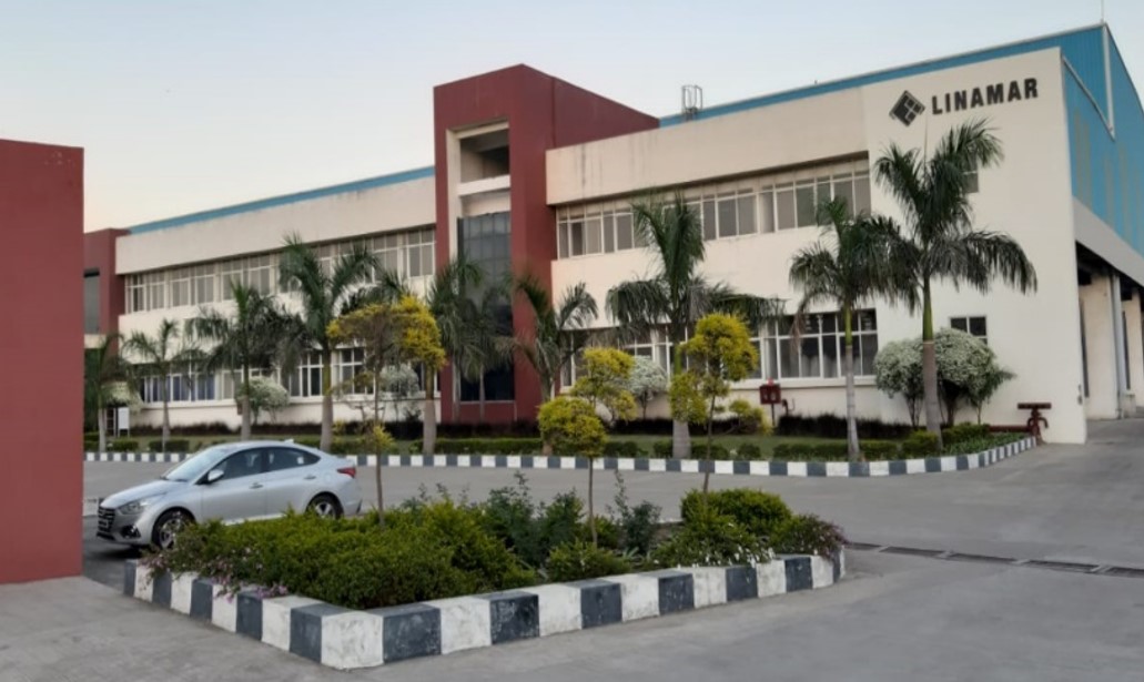 Modern multi-story office building with palm trees and parked cars in front, captured during daylight.