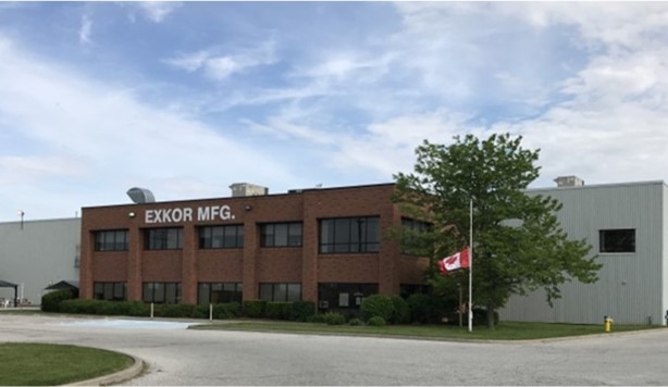 Exterior view of an Exxon Manufacturing industrial building with a parking lot and a Canadian flag in front.