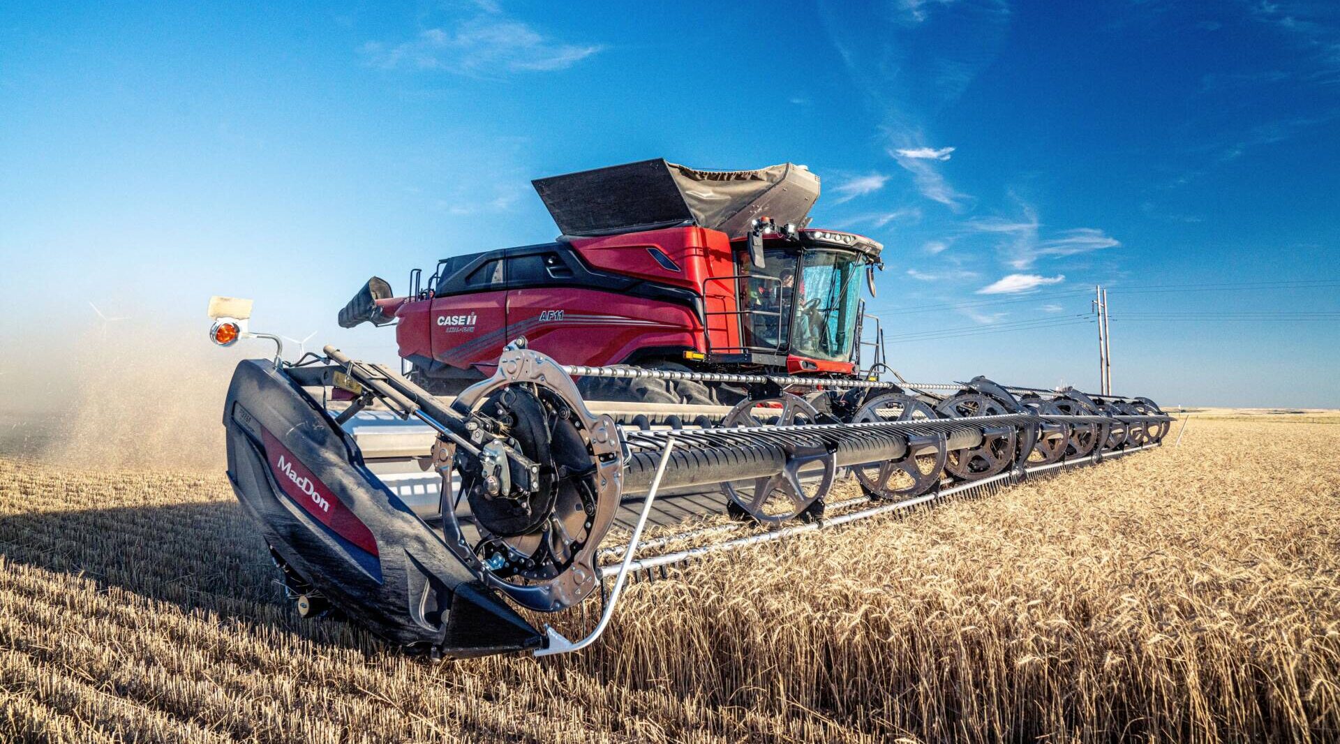 Red combine harvester operating in a golden wheat field under a clear blue sky.