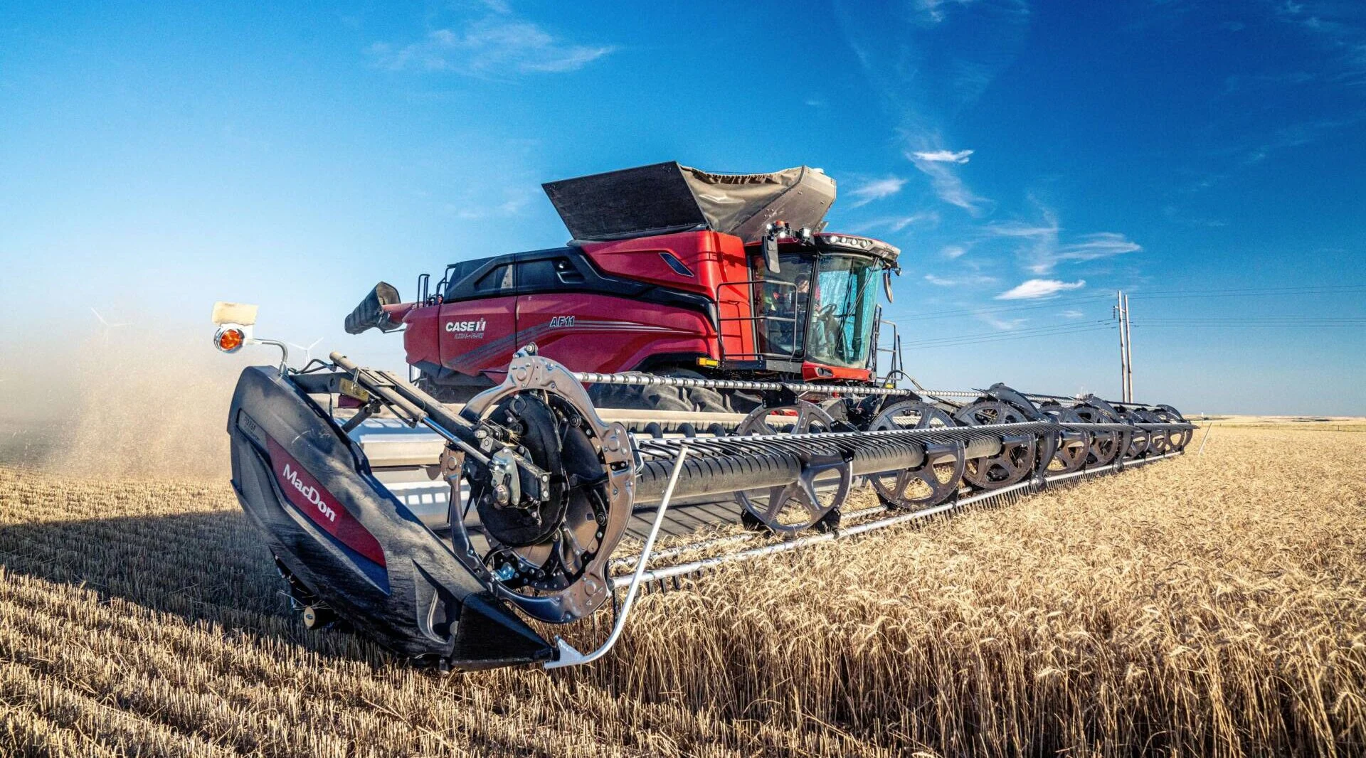 Red combine harvester operating in a golden wheat field under a clear blue sky.