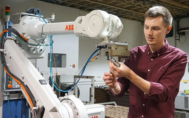 Man programming an industrial robotic arm in a modern factory setting.