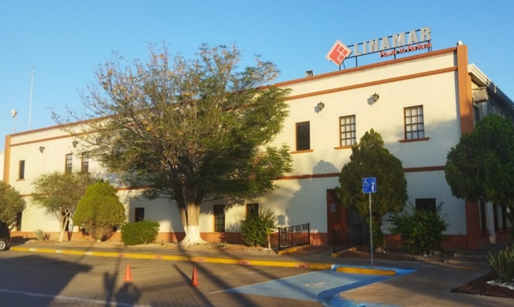 Front view of a beige commercial building with bushes, trees, and handicap parking spaces in front under a clear sky.