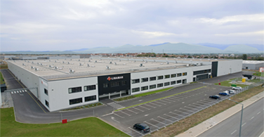 Aerial view of a large industrial warehouse facility with multiple loading docks and a spacious parking lot under a cloudy sky.