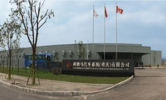 Exterior view of a modern industrial building with three flagpoles displaying flags and a large sign in front written in Chinese.
