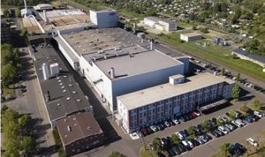 Aerial view of a large industrial manufacturing facility with adjacent parking lots and surrounding residential neighborhoods.