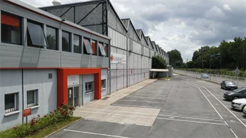 Exterior view of a modern industrial warehouse with parking spaces and a clear driveway under a cloudy sky.