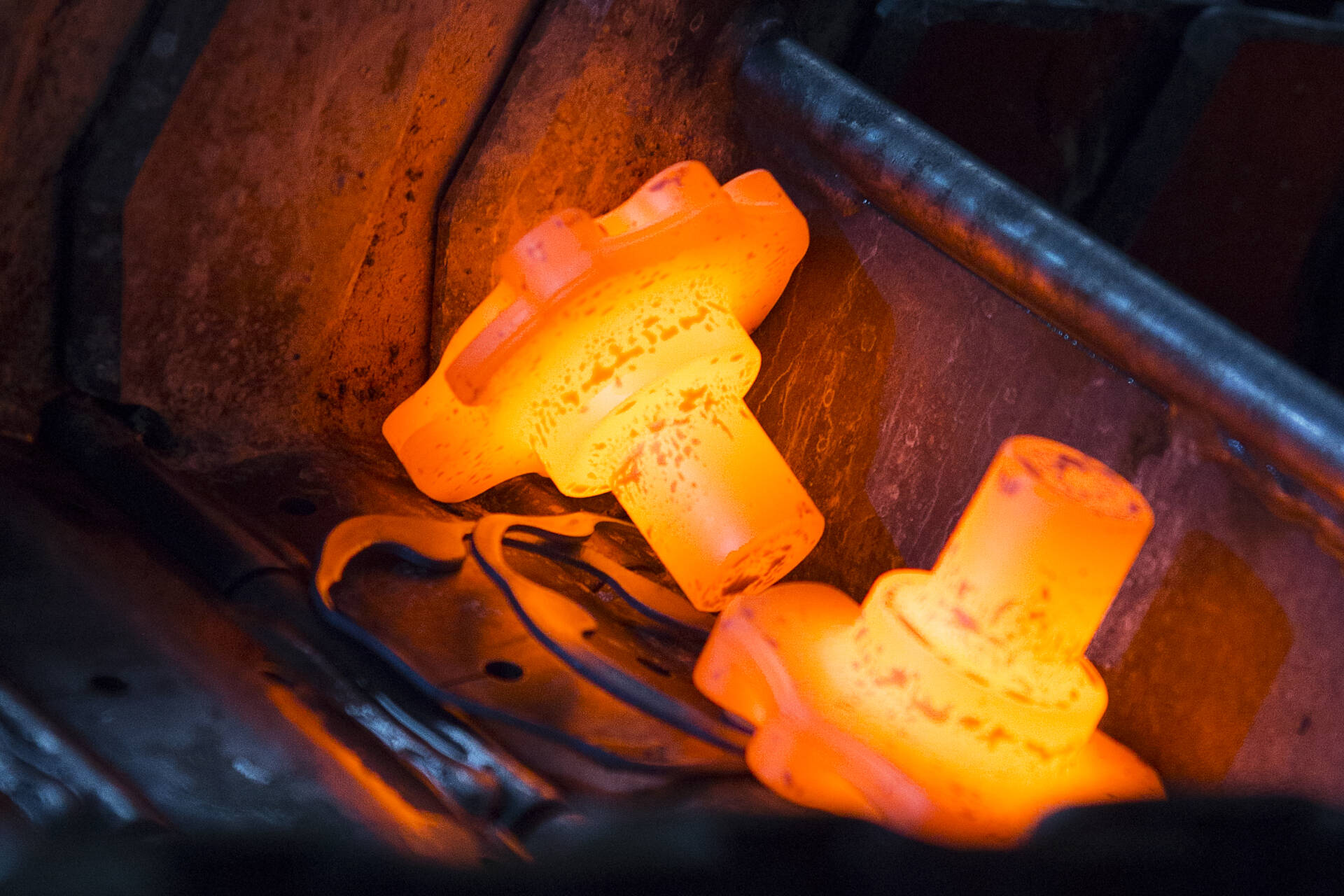 Two glowing orange hot metal gears being heated in an industrial furnace.