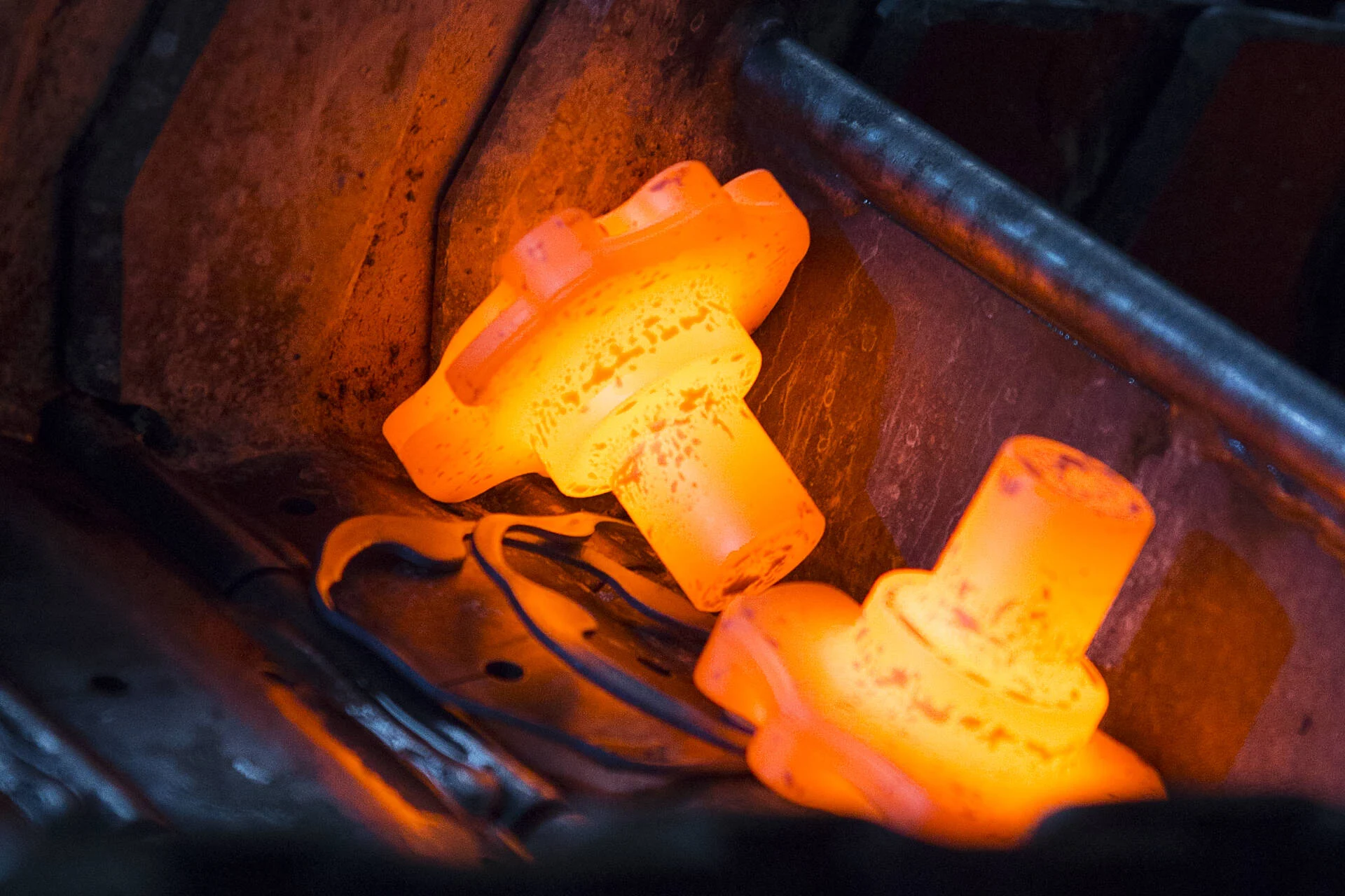 Two glowing orange hot metal gears being heated in an industrial furnace.