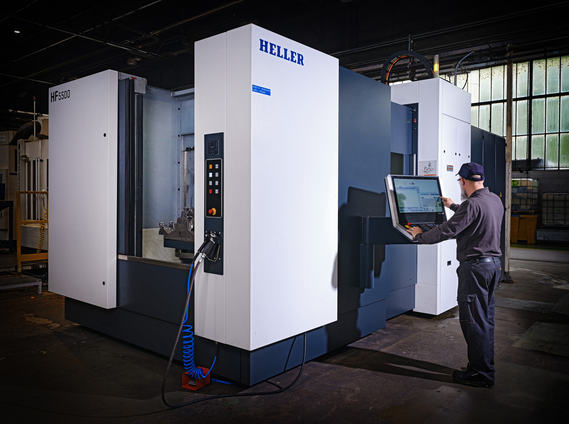 A technician operates a large HELLER industrial machine in a spacious, well-lit manufacturing facility.