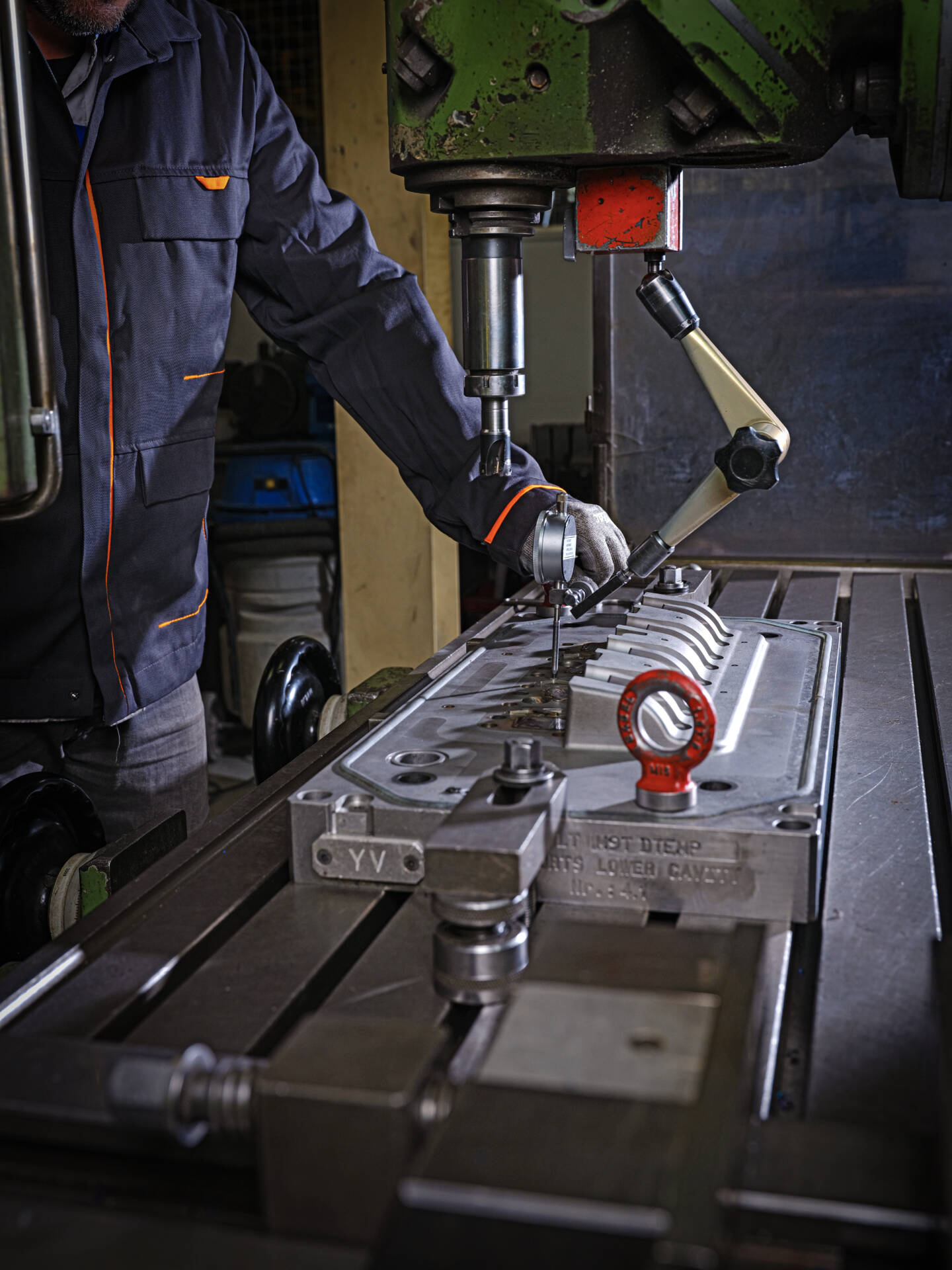 Close-up of a worker operating a drill press machine on a metal workpiece in an industrial workshop.
