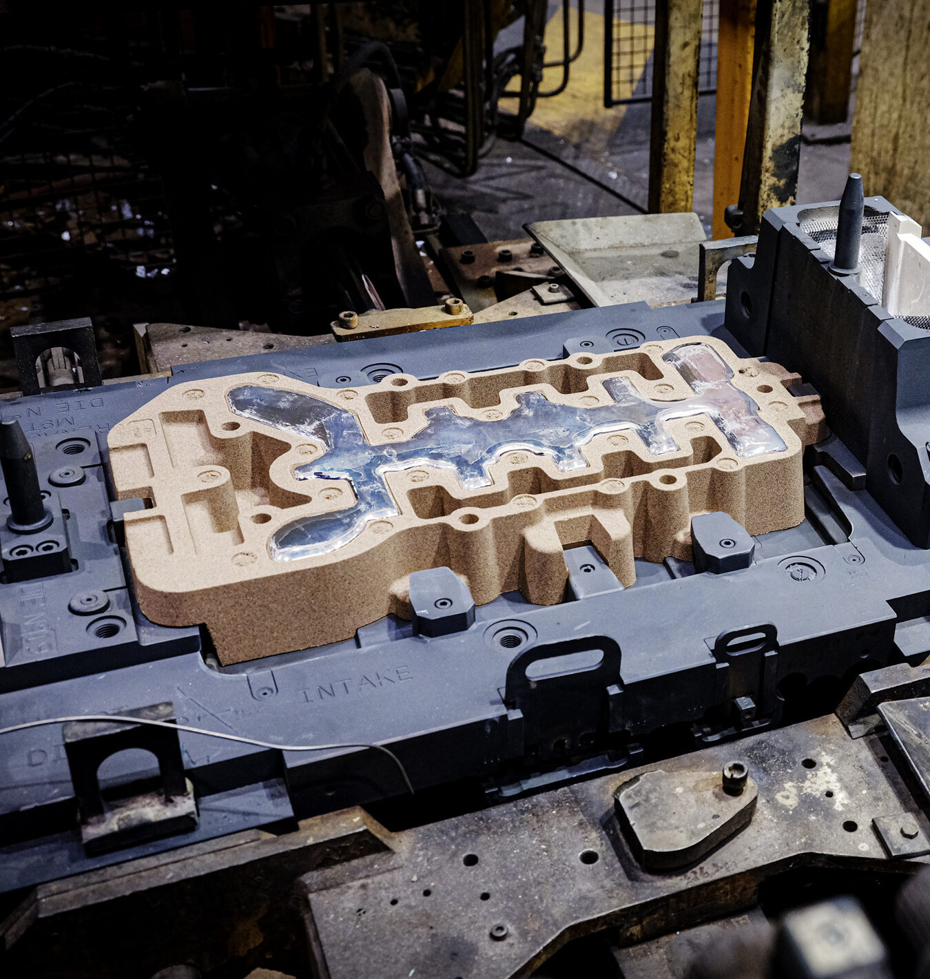 Close-up of a metal casting mold used in manufacturing, showing intricate cavity details on an industrial machine platform.
