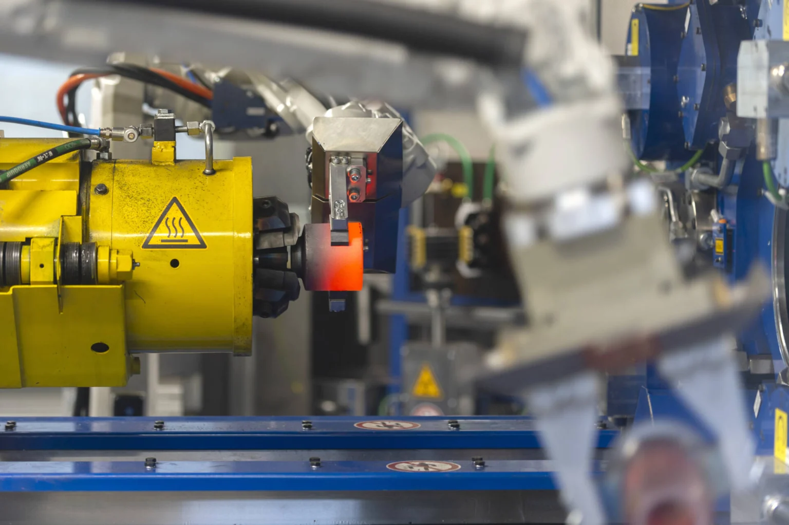 Close-up of automated industrial machinery operating in a manufacturing facility, focusing on a robotic arm and conveyor system.