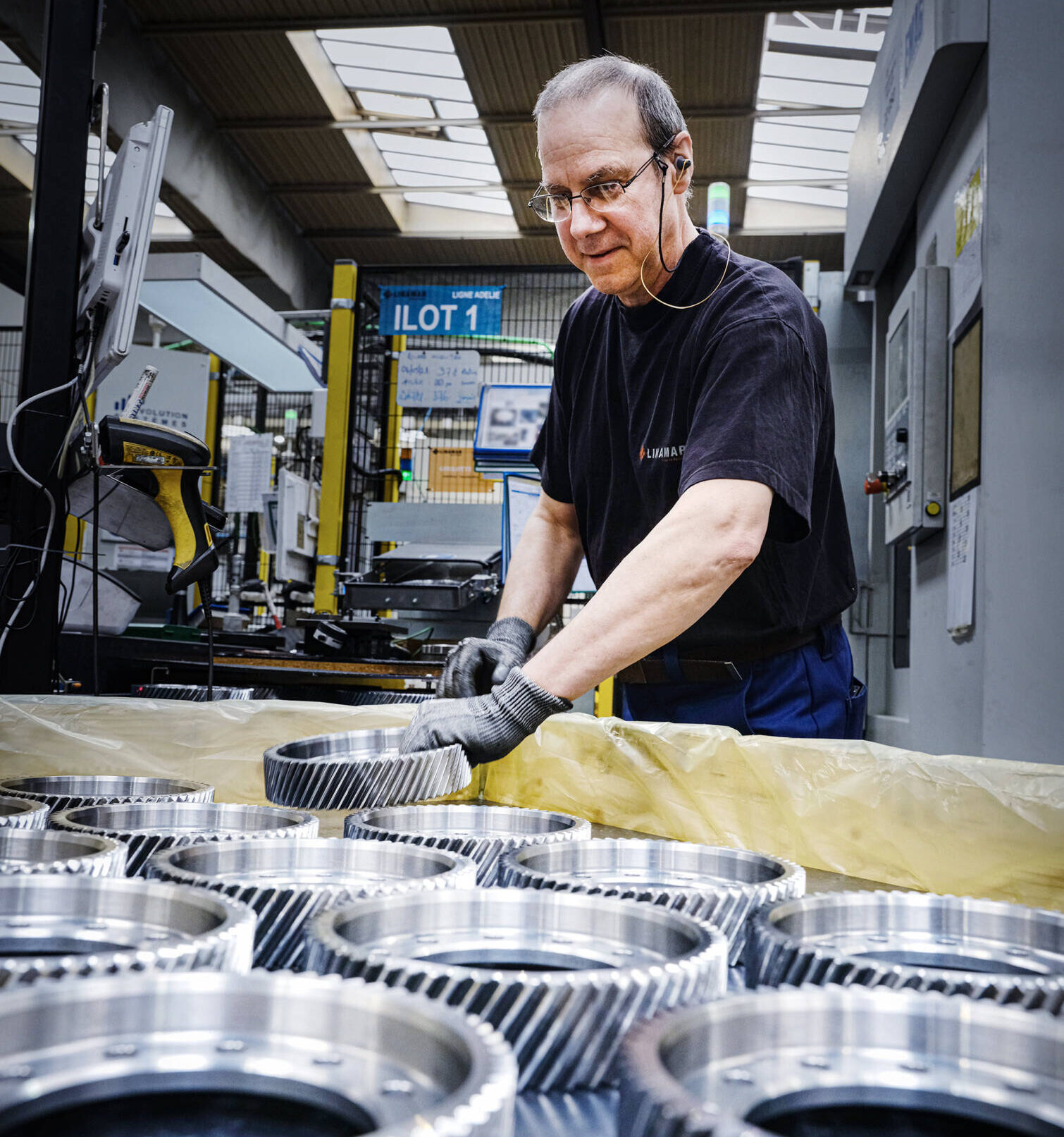 Factory worker inspecting metal gears on an assembly line in an industrial manufacturing facility.
