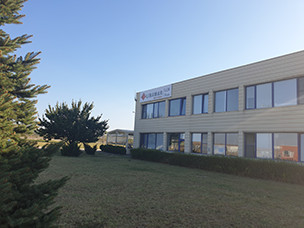 Exterior view of a modern two-story office building with large windows and a well-maintained lawn under a clear blue sky.
