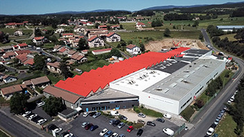 Aerial view of a large industrial warehouse with a red roof adjacent to a residential neighborhood and surrounded by roads and parking lots.