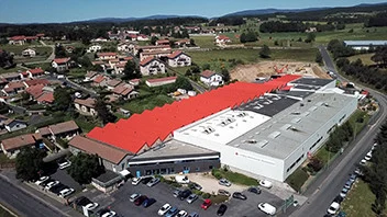 Aerial view of a large industrial warehouse with a red roof adjacent to a residential neighborhood and surrounded by roads and parking lots.