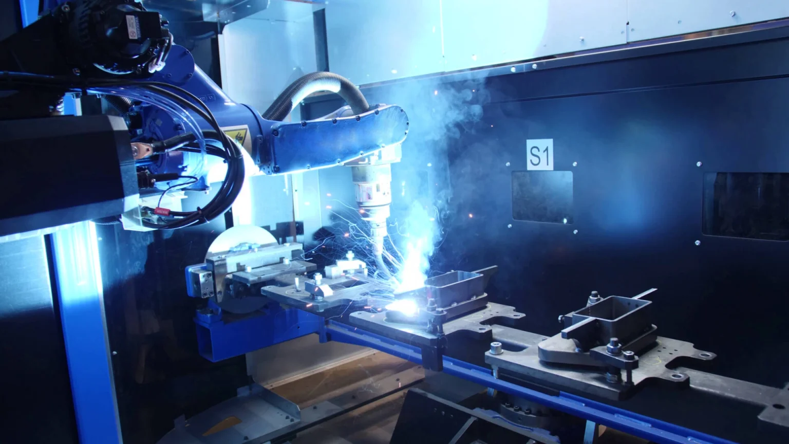 Robotic welding machine performing automated metal fabrication with bright welding sparks in an industrial setting.