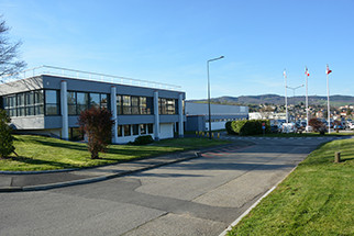Modern office building with large windows situated along a paved road and green lawns under a clear blue sky.