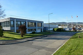 Modern office building with large windows situated along a paved road and green lawns under a clear blue sky.