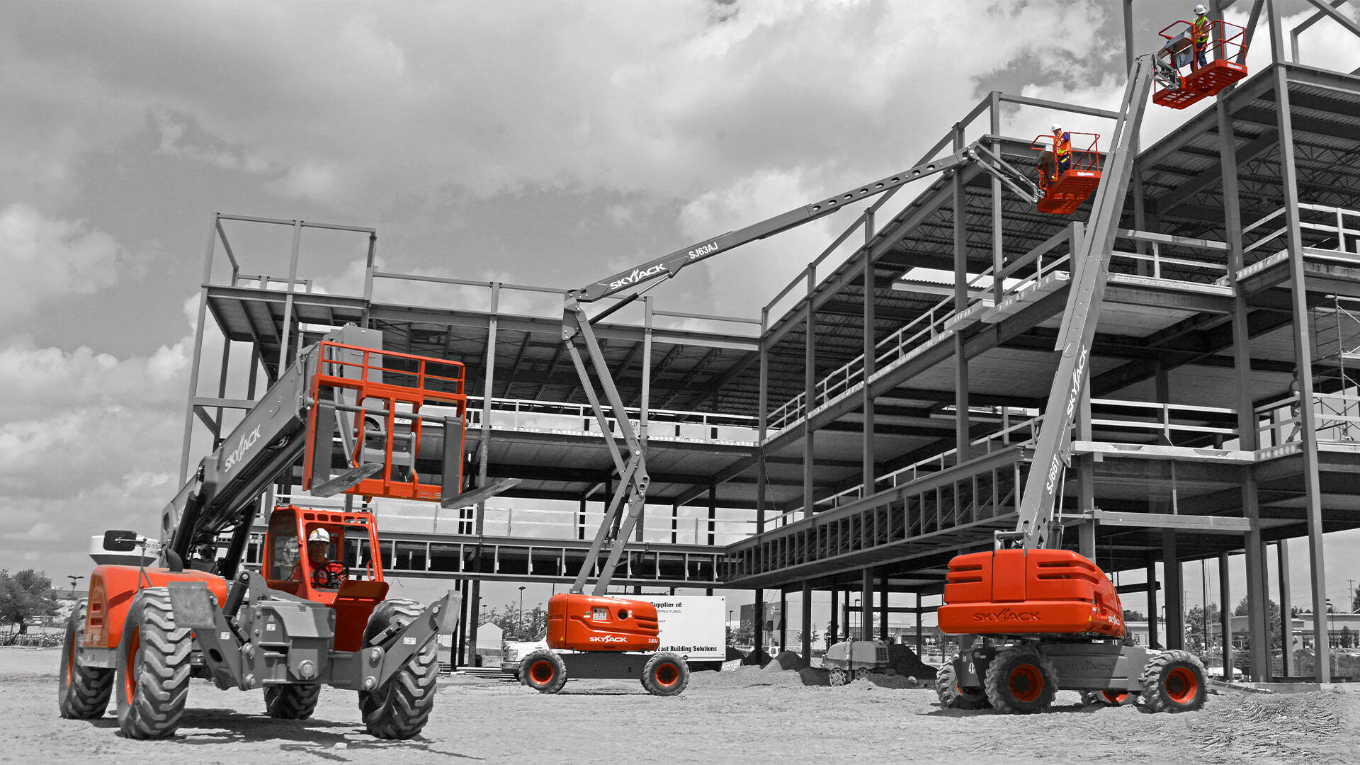 Black and white image of a construction site featuring steel framework and several orange boom lifts actively positioned around the structure.