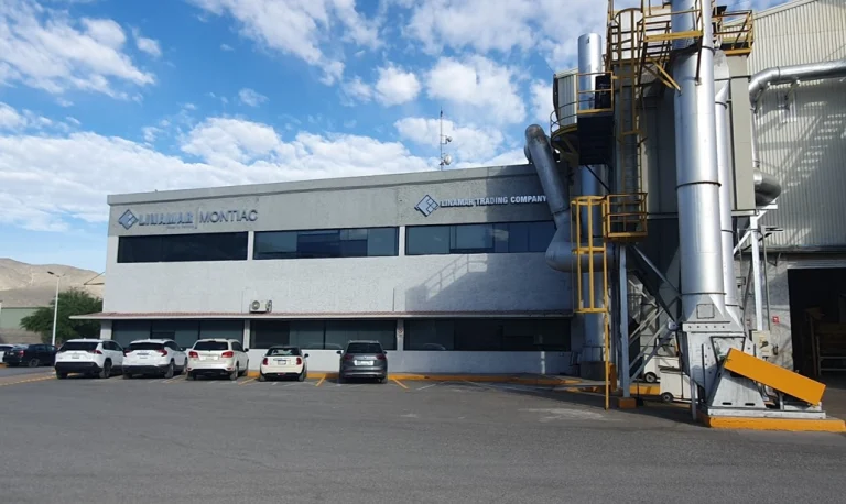 Exterior view of a commercial industrial building with parked vehicles under a partly cloudy sky.