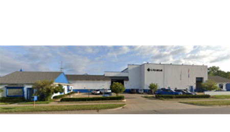 Exterior view of a Polaris manufacturing facility with company vehicles parked outside under a partly cloudy sky.