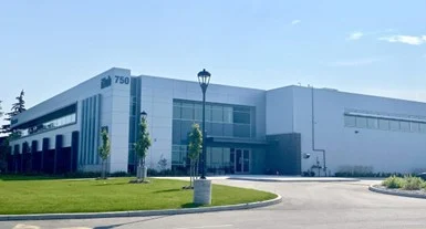 Modern white industrial building with large windows and a well-maintained lawn under a clear blue sky.